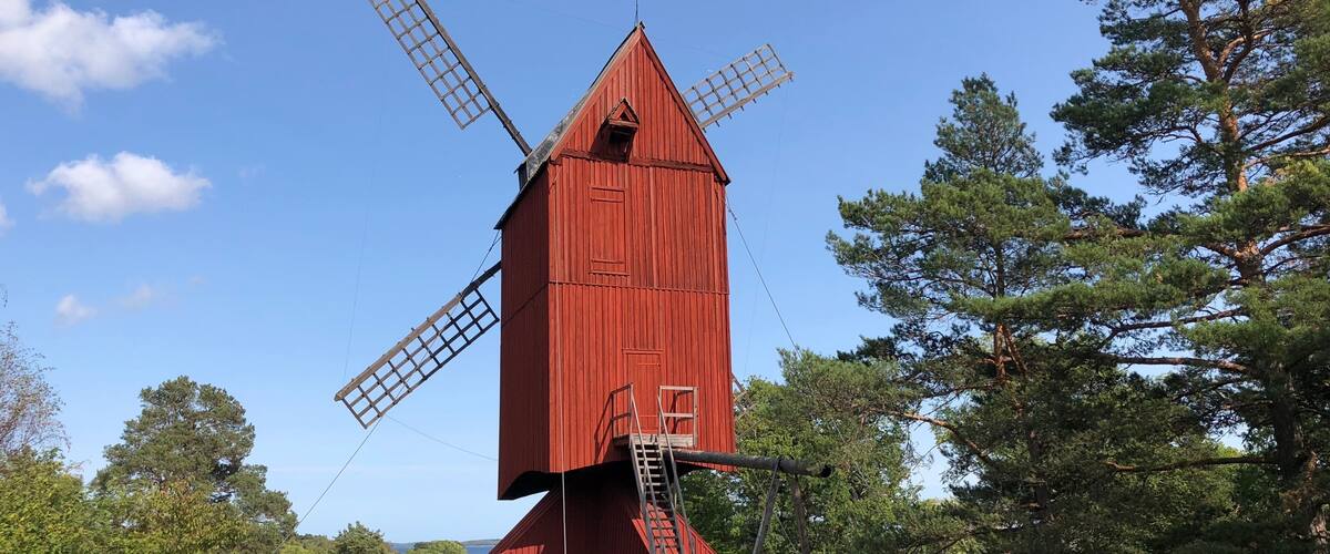A red windmill with two large sails, surrounded by trees and a clear sky.