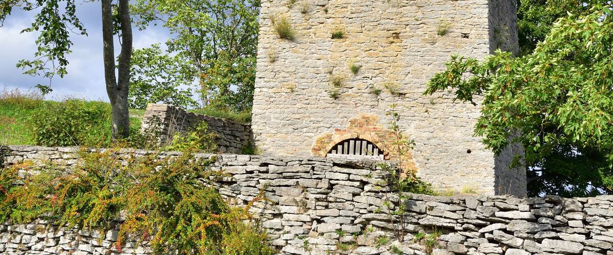 A stone structure with a conical chimney and a stone wall with vegetation.