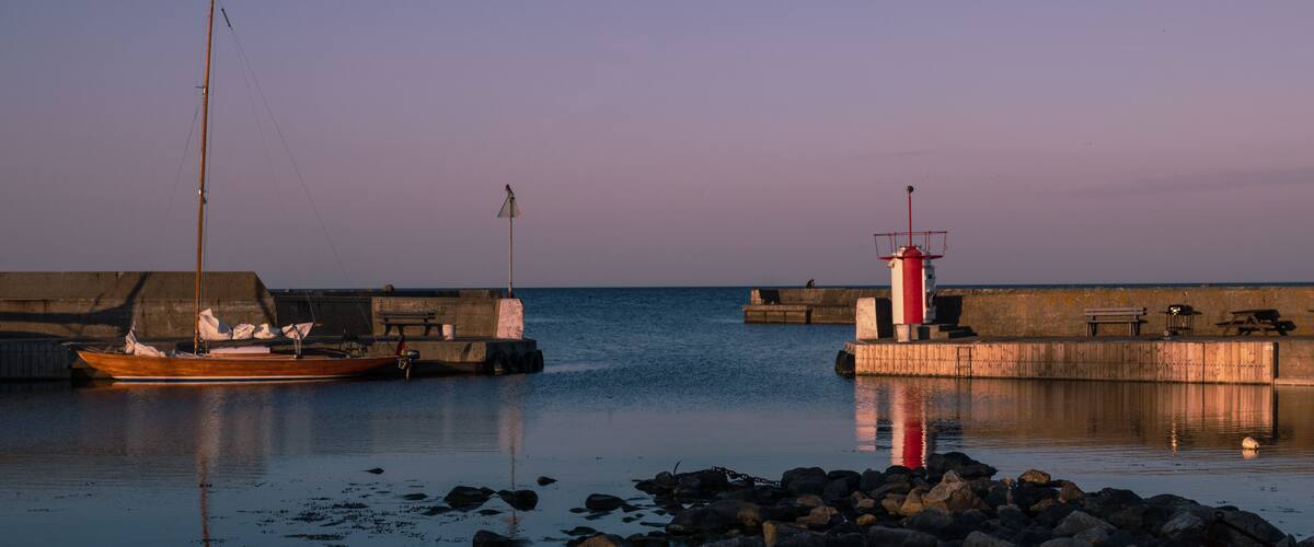 A calm harbor with a wooden boat, a red lighthouse, and a rocky shoreline.