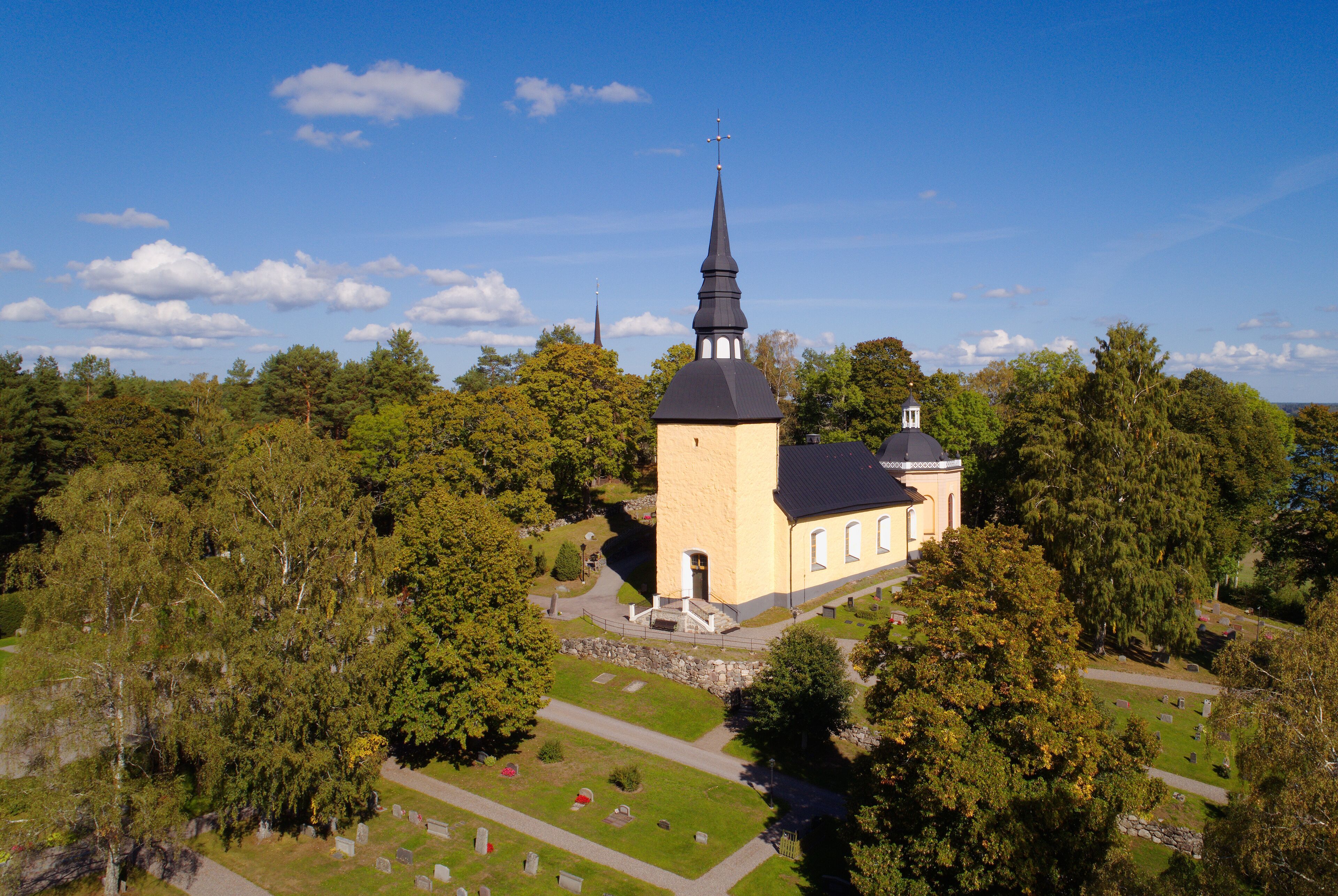 A church with a tall spire surrounded by trees and a cemetery.
