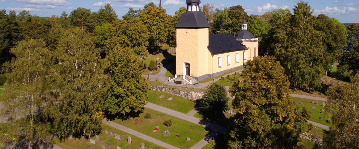 A church with a tall spire surrounded by trees and a cemetery.