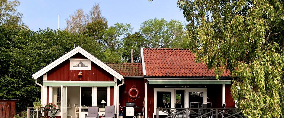 A wooden dock leading to a red and white building with a red roof, surrounded by greenery.
