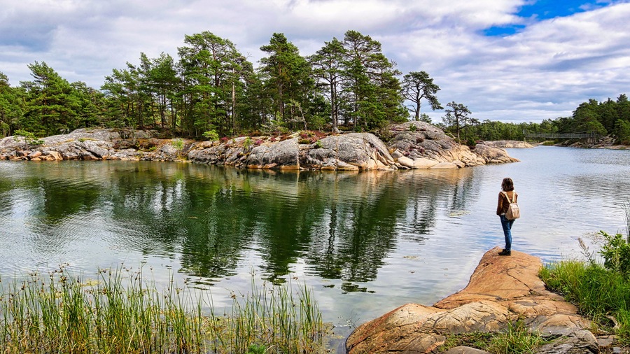 Wanderin beobachtet auf einer Felskuppe die gegenüberliegende Schäreninsel im Naturreservat Stendörren in Schweden