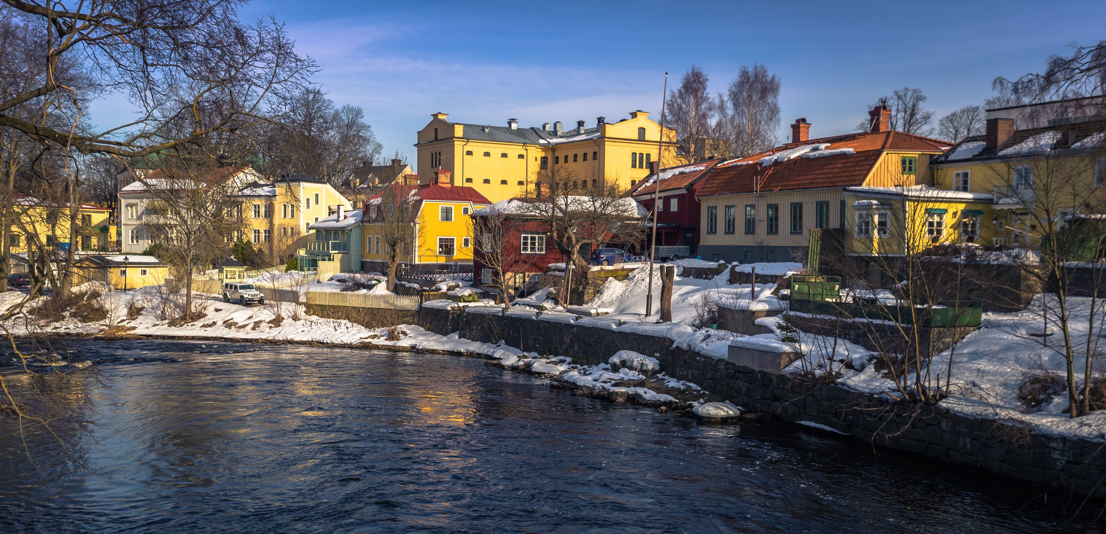 A river with snow-covered banks and colorful buildings along the shore.
