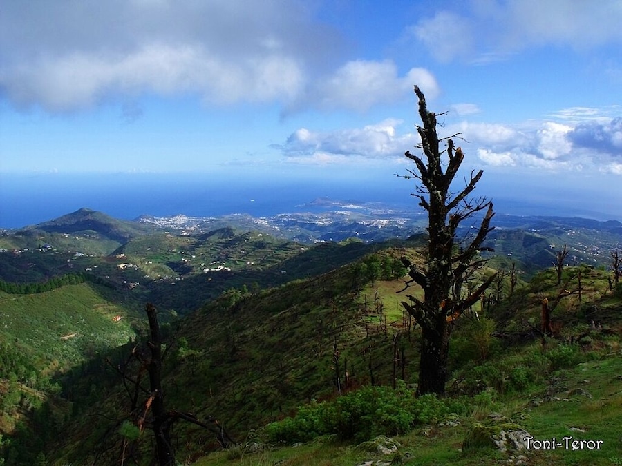 Paisaje montañoso con vista despejada al océano y pueblos lejanos.