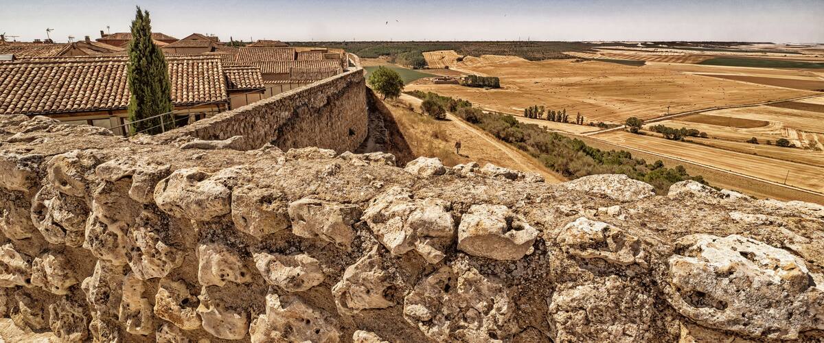A stone wall with a view of terraced fields and a traditional tiled-roof building.