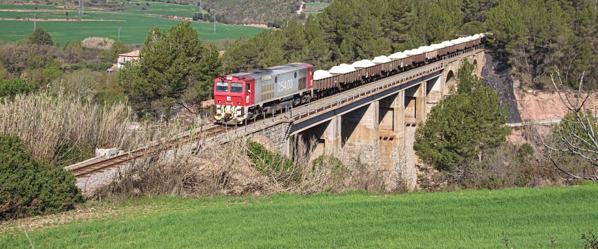 A train crossing a stone bridge over a river in a hilly landscape.