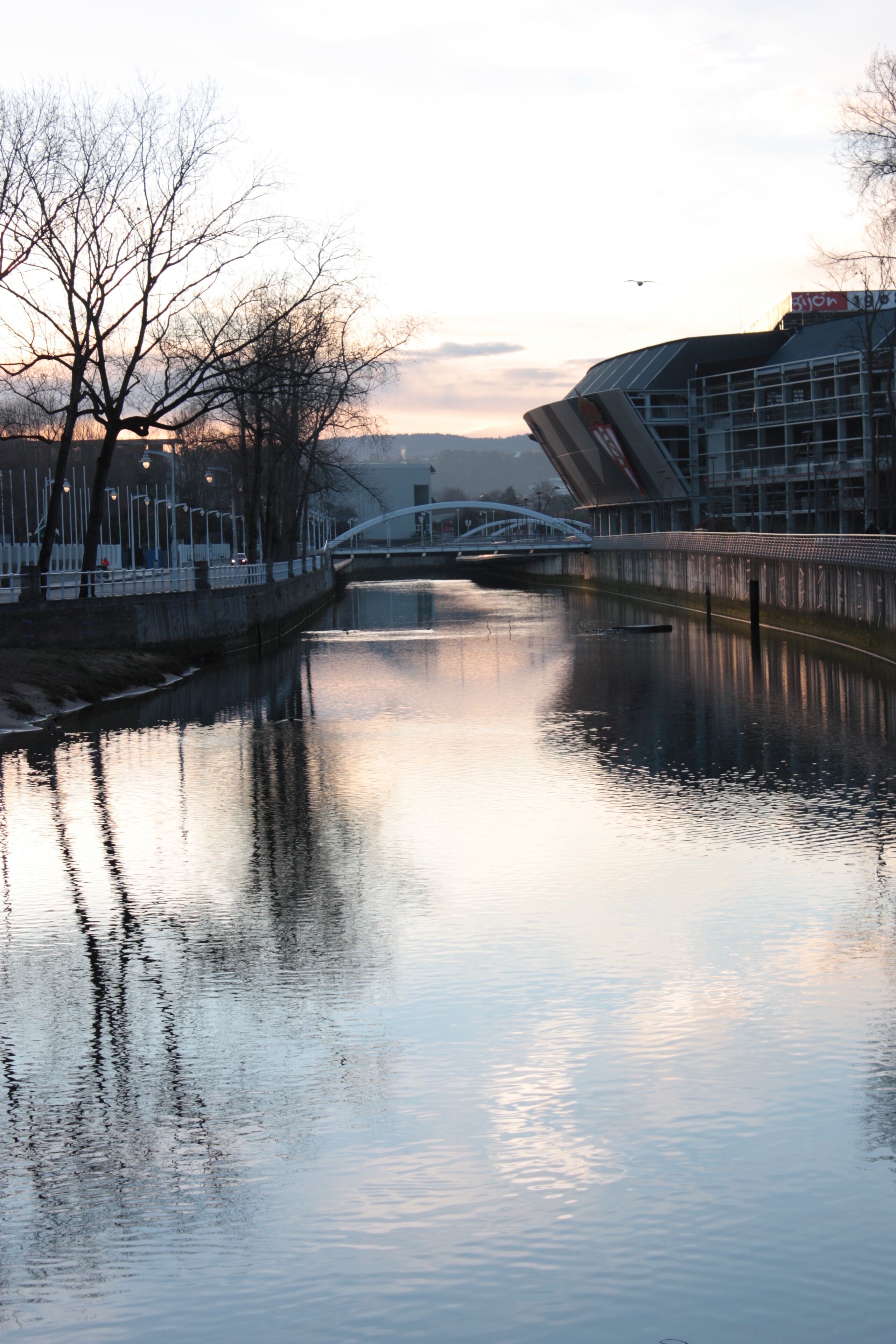A calm river with a bridge and buildings in the background.