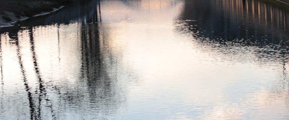 A calm river with a bridge and buildings in the background.