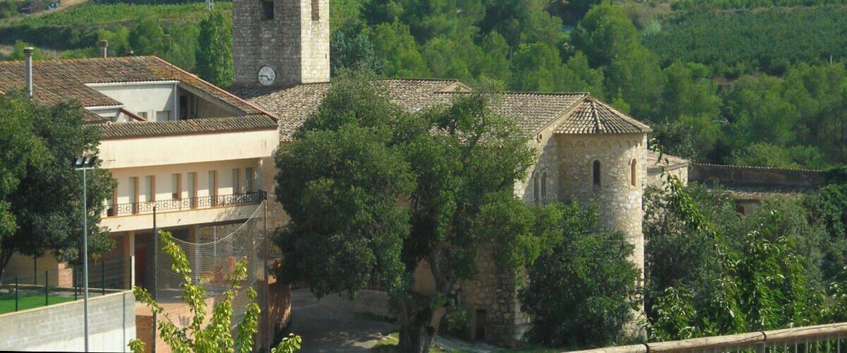 A rural landscape with a stone church featuring a bell tower, surrounded by lush greenery and rolling hills.