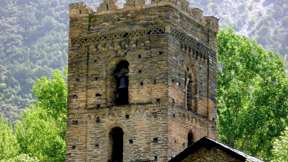 A medieval stone tower with battlements, surrounded by lush green trees and a mountainous backdrop.