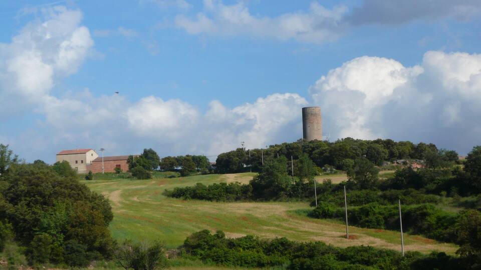 A tower on a hill, a building with a red roof, and a grassy landscape with trees.