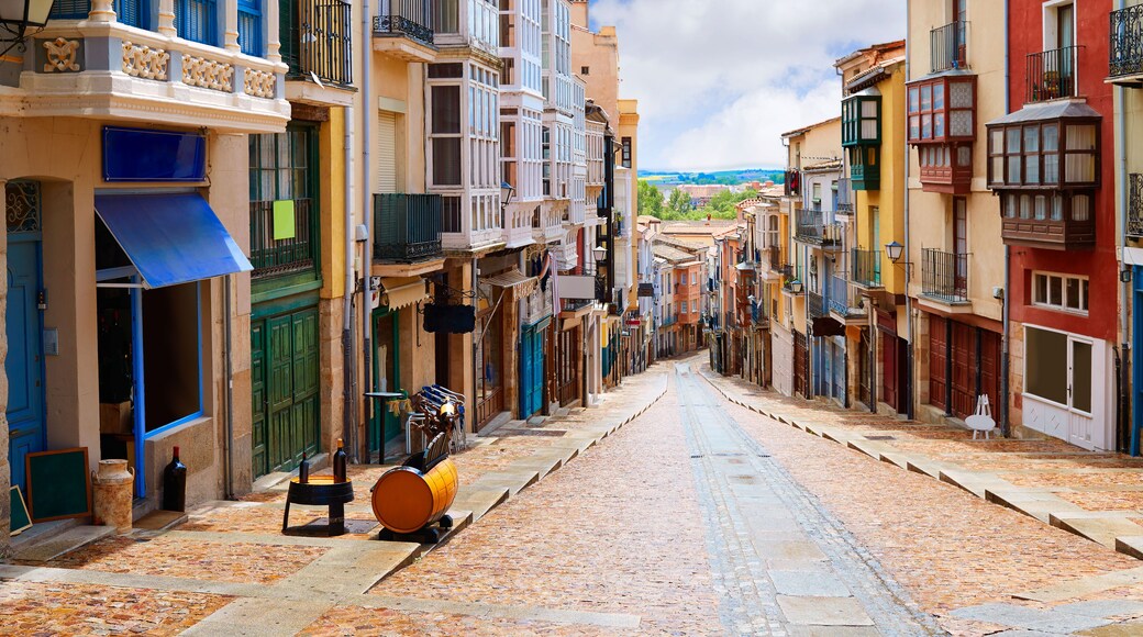 A cobblestone street lined with colorful buildings, a yellow barrel, and a blue awning.