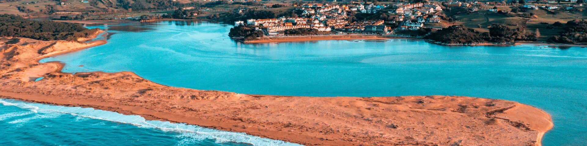 A drone photo capturing Liencres Beach and the Pas River estuary, showcasing turquoise waters, golden sand formations, and the surrounding natural reserve in Cantabria (Spain).