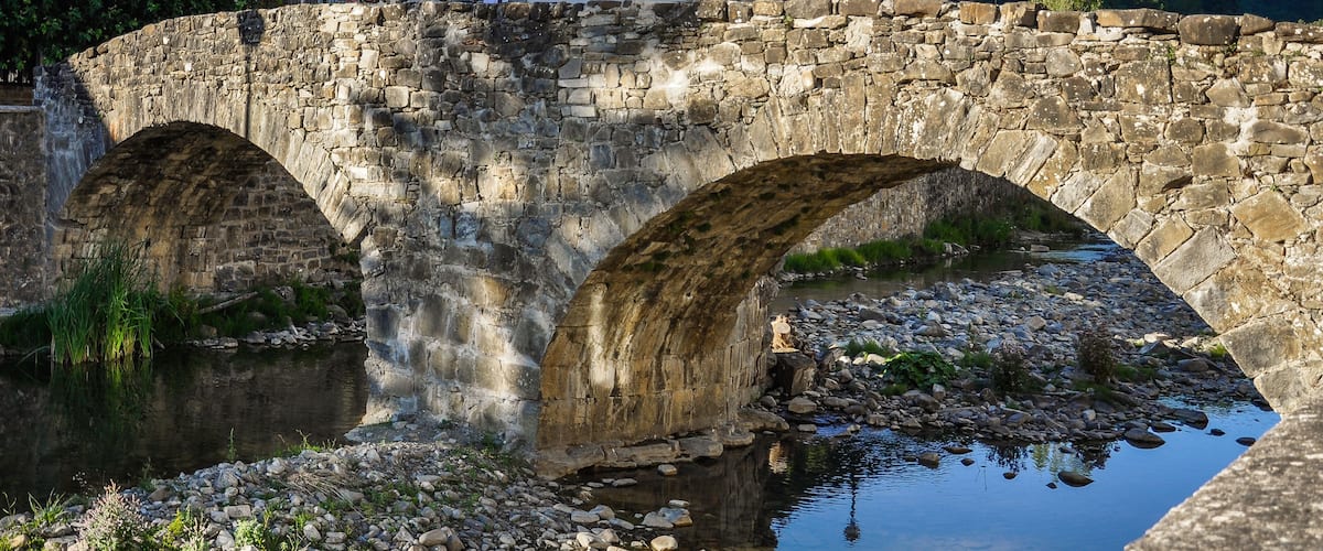 A stone bridge over a river with a small statue on the right side.