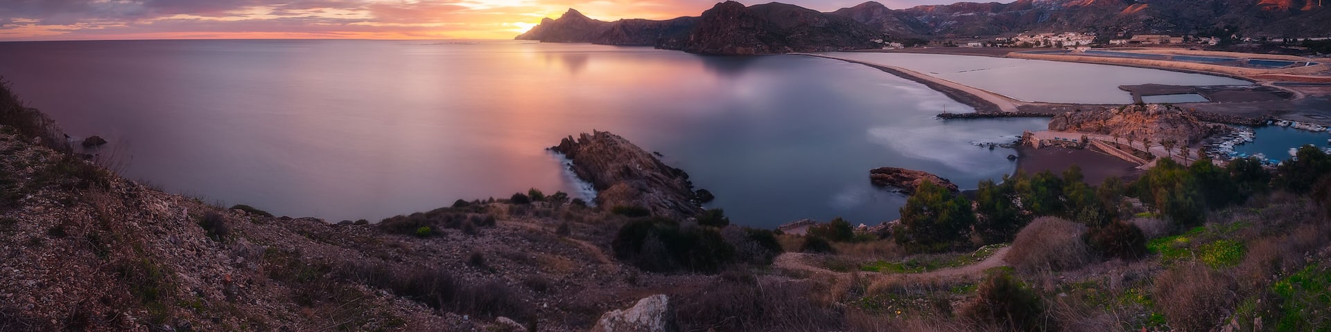 A coastal landscape with a sunset, rocky terrain, and a calm sea.