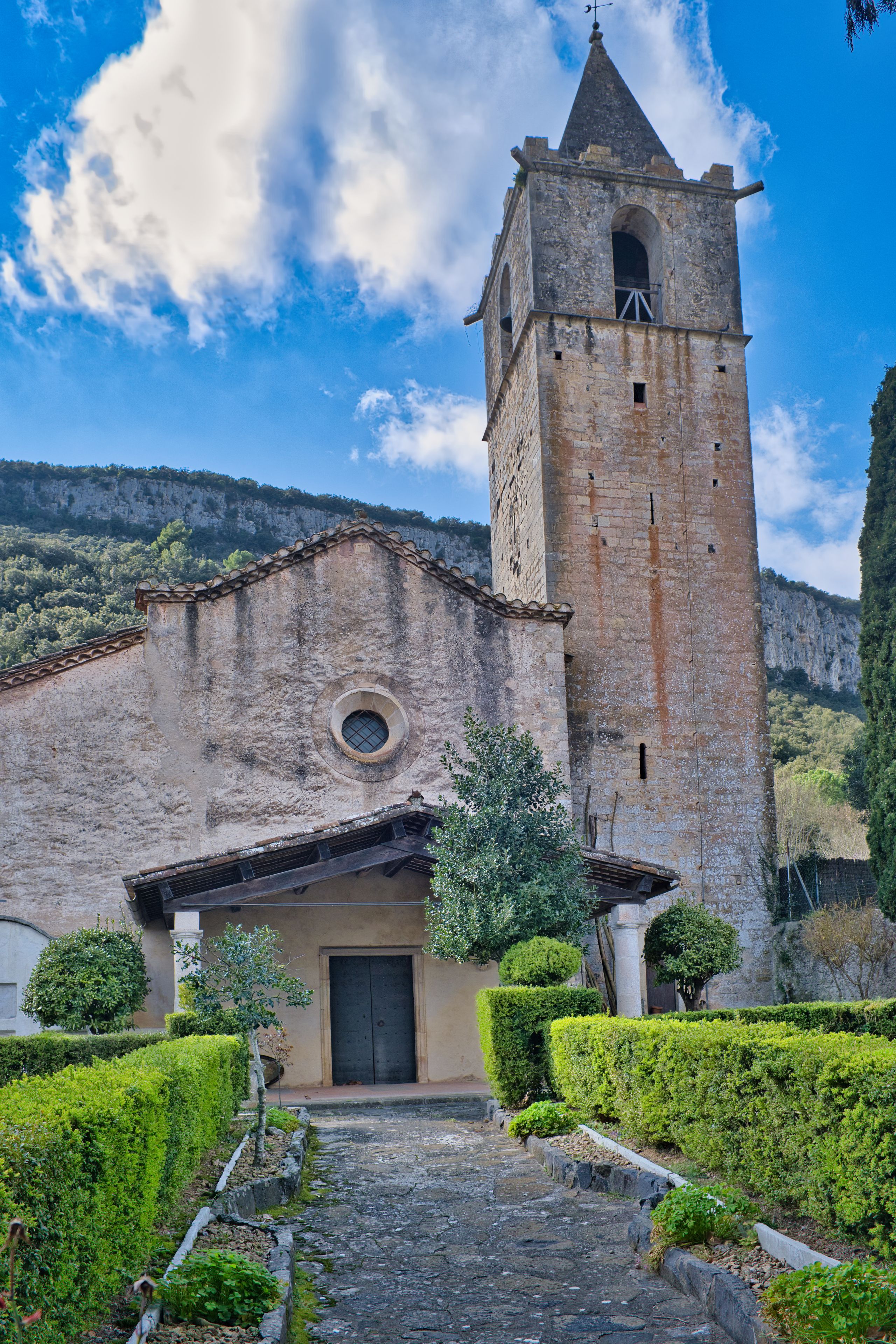 Una iglesia histórica con un campanario, rodeada de setos cuidados y un camino adoquinado.