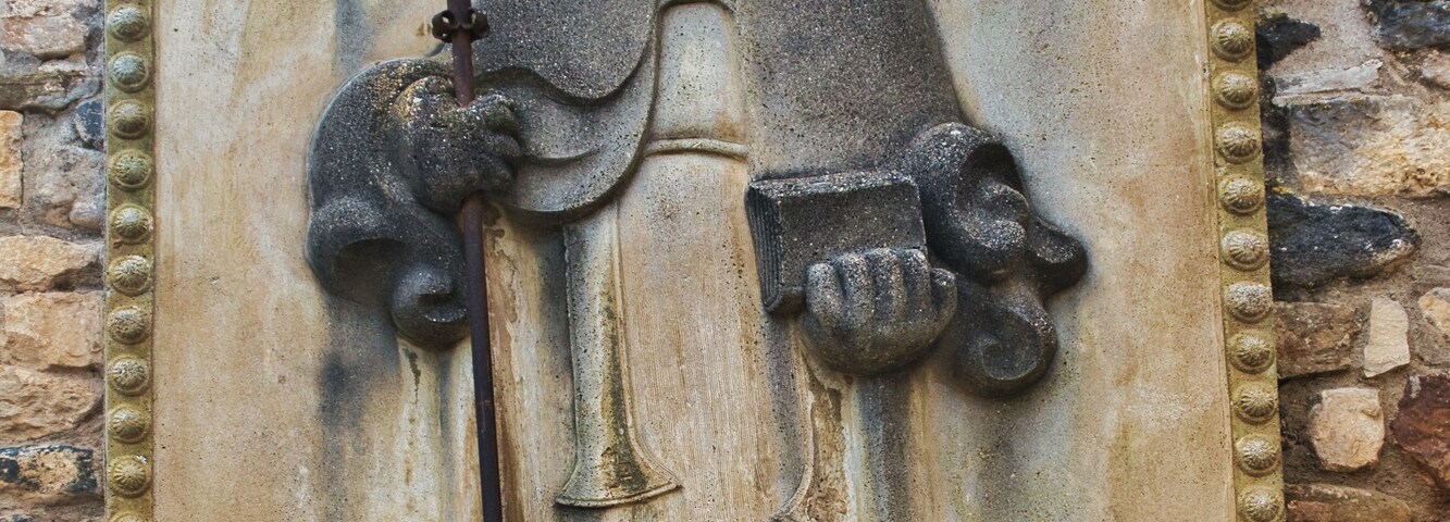 Relevo de pedra de uma figura segurando um cajado, com inscrições e uma base.