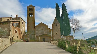 A stone church with a bell tower, surrounded by stone buildings and tall cypress trees.