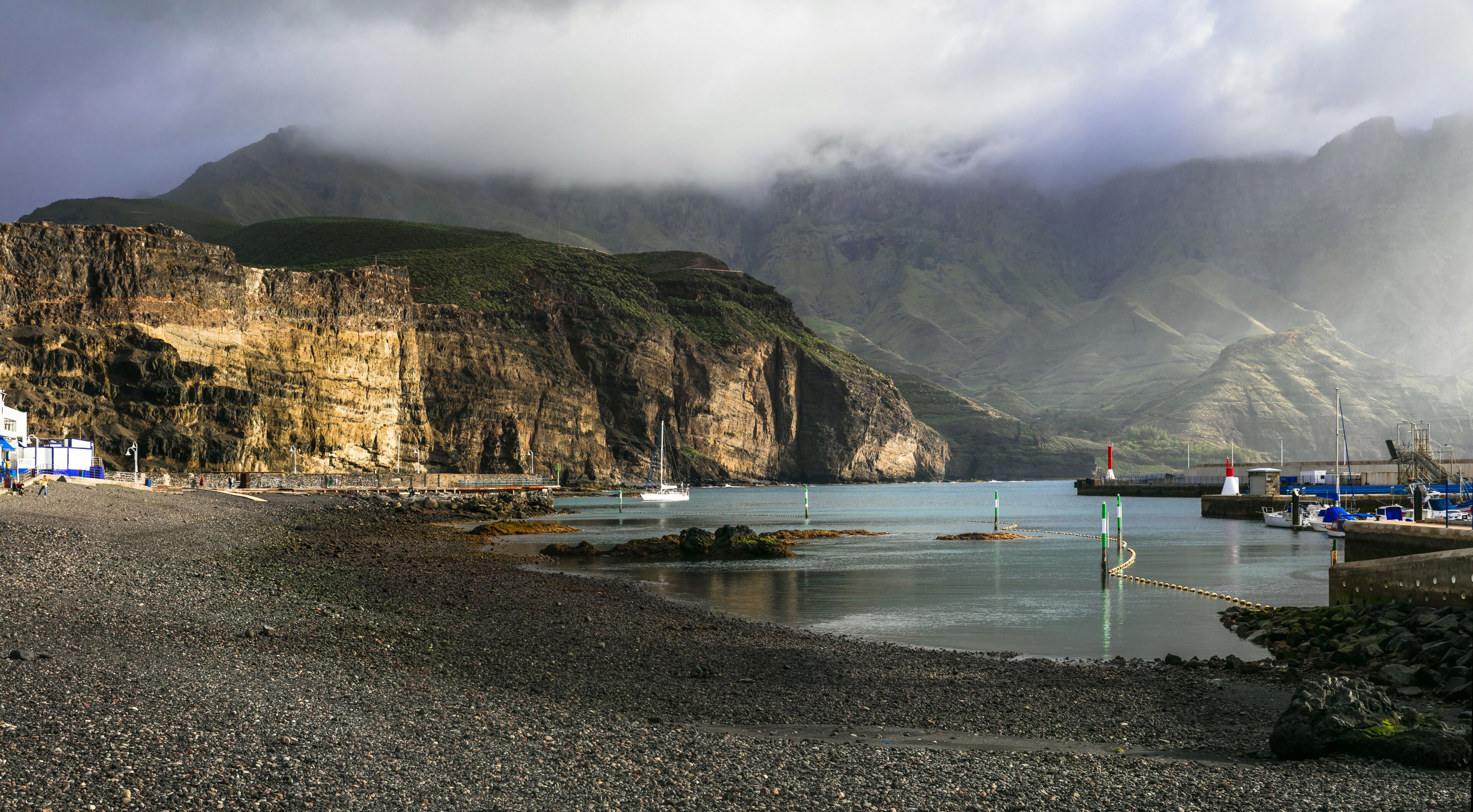 A rocky beach with a lighthouse, boats, and a mountainous backdrop.