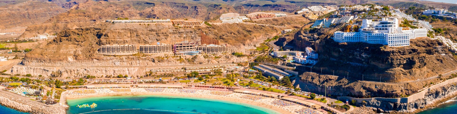 Un complejo turístico frente al mar con una piscina grande, una playa y edificios en un acantilado.