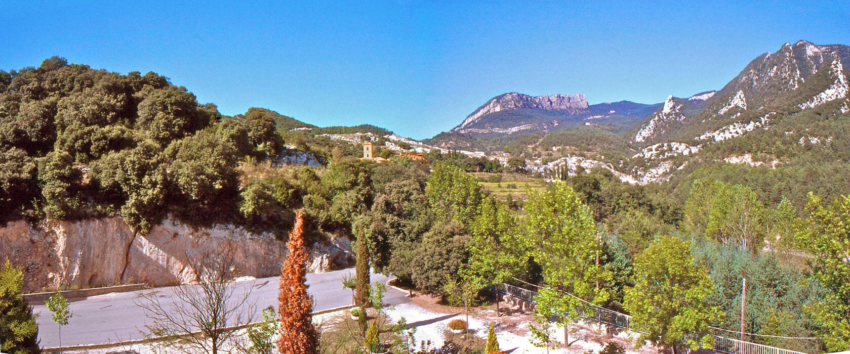 A mountainous landscape with a road, trees, and a small tower.