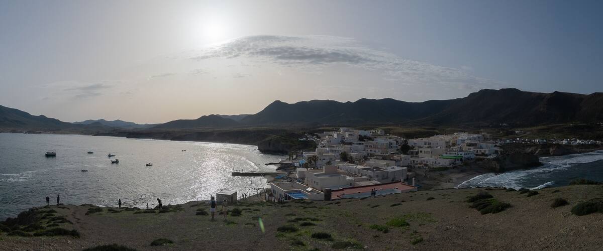 A coastal town with buildings near the sea, boats on the water, and mountains in the background.
