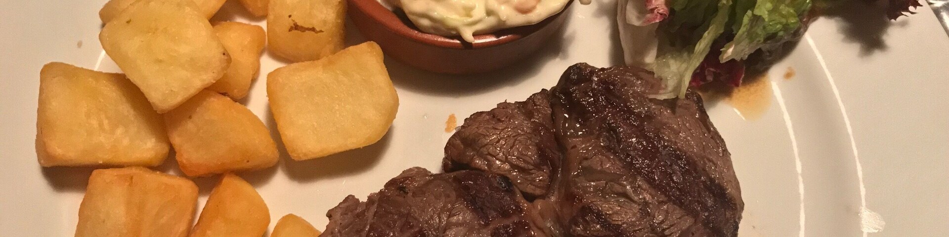 A plate with a steak, potato wedges, a creamy salad, and a side of mixed greens.