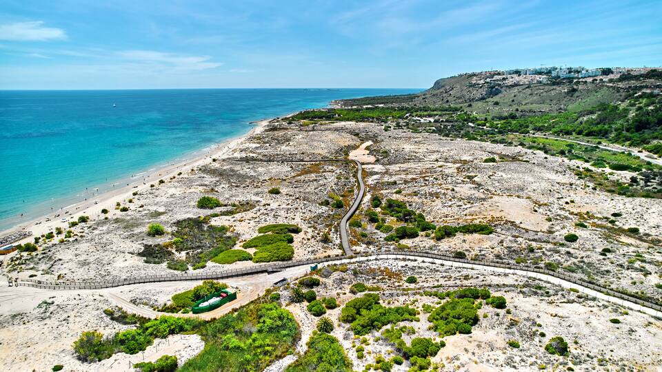 A coastal landscape with a beach, rocky terrain, and a winding road leading to a settlement.