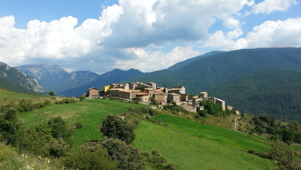 A historic village nestled in a valley with mountains in the background.