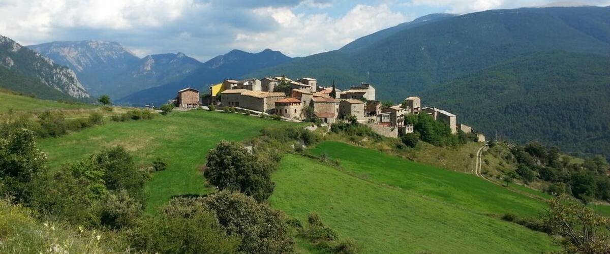 A historic village nestled in a valley with mountains in the background.