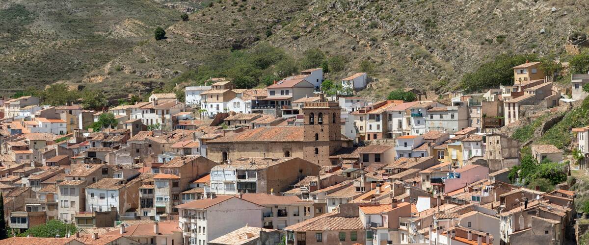A densely packed hillside town with terracotta-roofed buildings and a prominent tower.