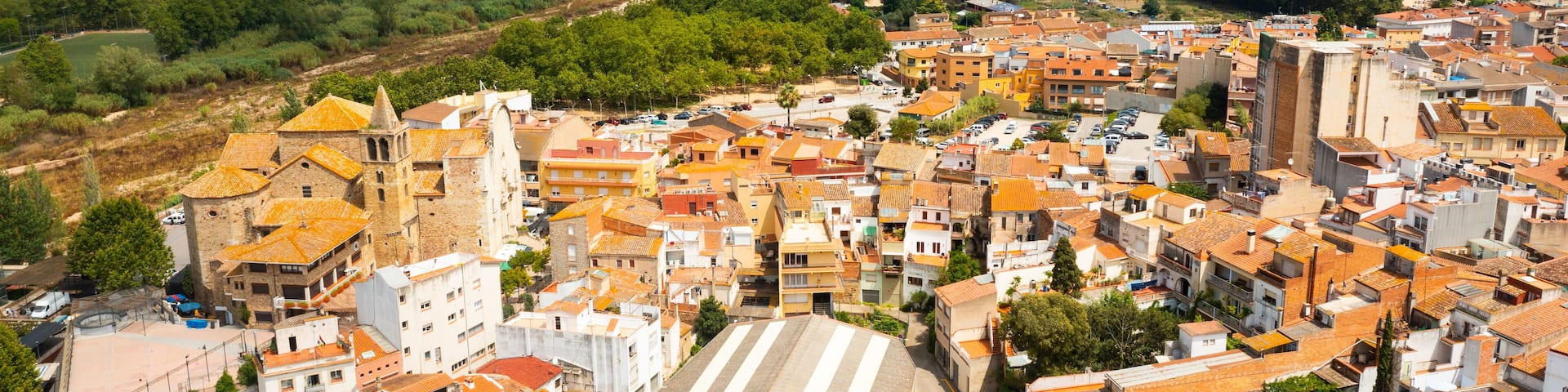 Scenic summer view of tiled roofs of residential houses of Spanish township of Tordera on background of greenery of Montnegre natural park on horizon on sunny day, province of Barcelona, Catalonia