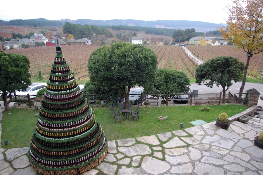 A large Christmas tree made of wine bottles, a stone patio, and a vineyard in the background.