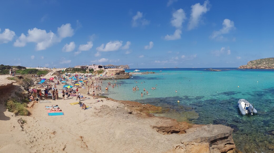 San Antonio, Ibiza - 07/14/2018: Panoramic view of Cala Comte beach in Spain during summer with a crispy clear turquoise sea water and people laying down on the sand beach