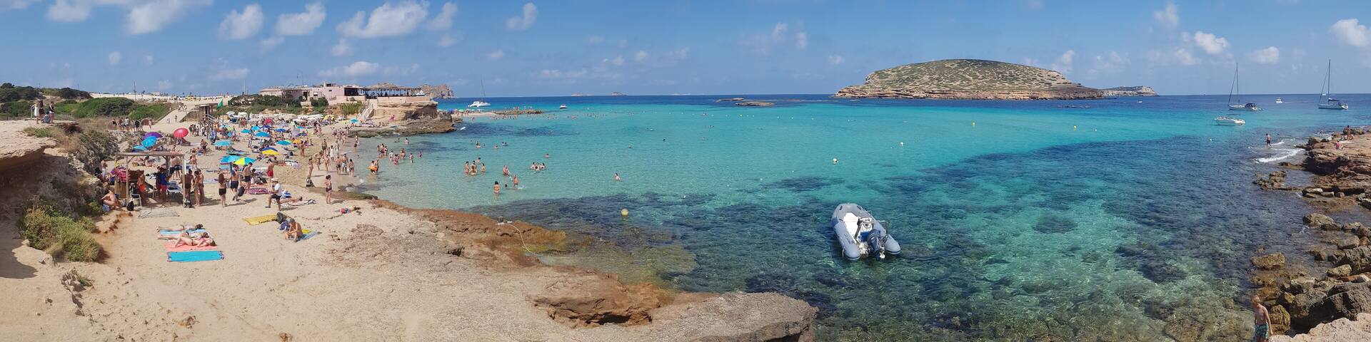 San Antonio, Ibiza - 07/14/2018: Panoramic view of Cala Comte beach in Spain during summer with a crispy clear turquoise sea water and people laying down on the sand beach