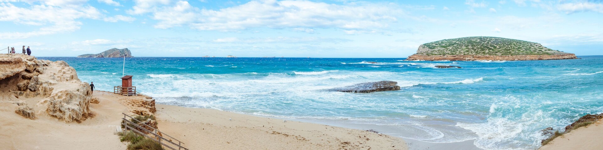 Una playa con olas, un promontorio rocoso y una pequeña isla.