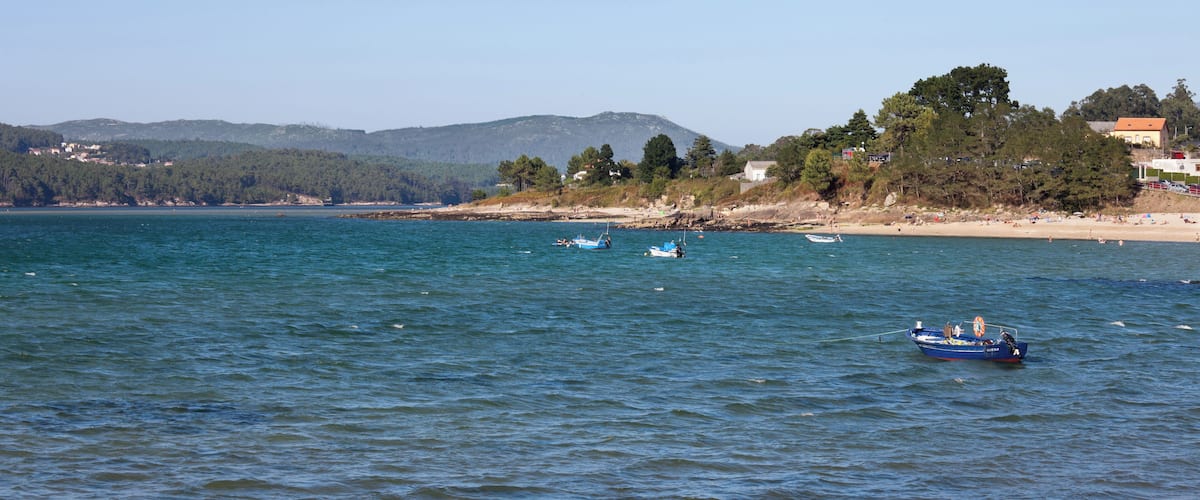 A coastal scene with calm waters, a sandy beach, and a backdrop of hills and trees.