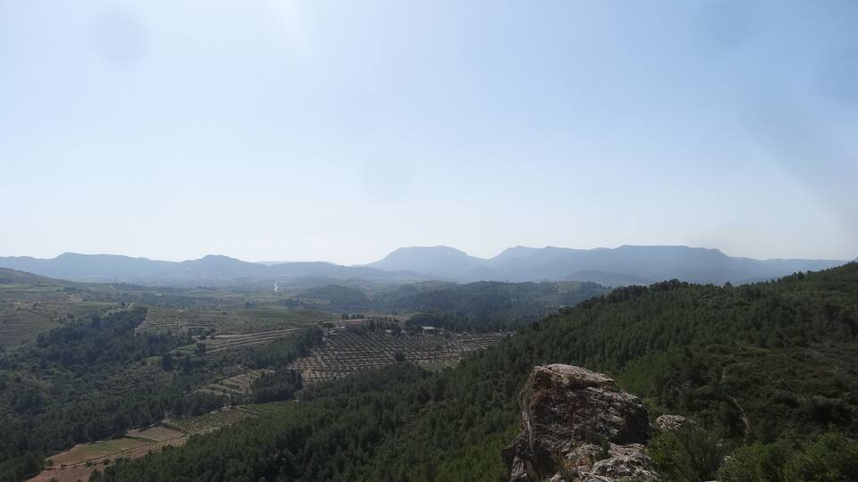 A mountainous landscape with dense forests, terraced fields, and distant mountains under a clear sky.