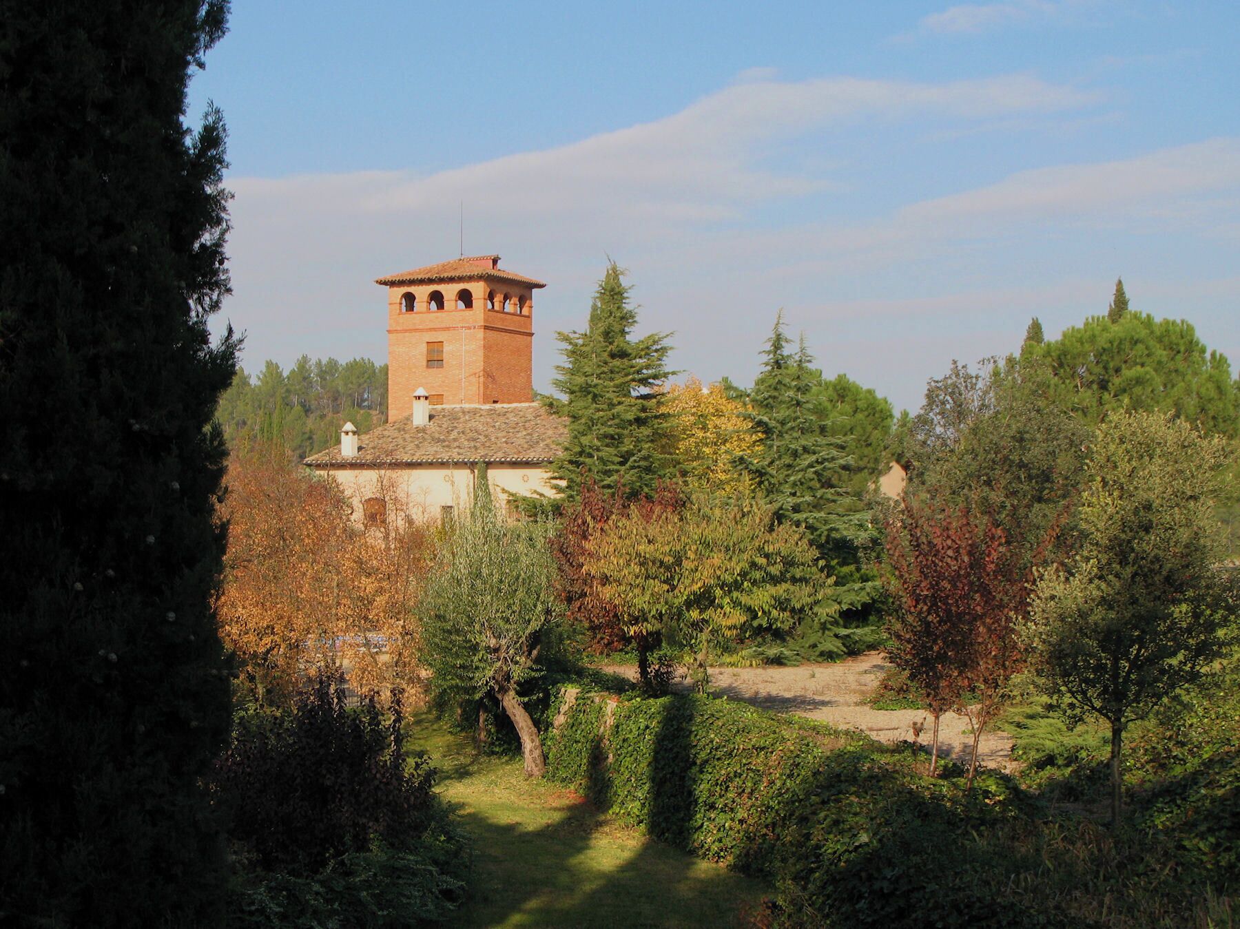 A tower with a red roof and arched windows, surrounded by trees and a hedge.