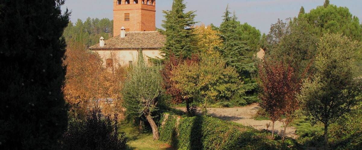 A tower with a red roof and arched windows, surrounded by trees and a hedge.