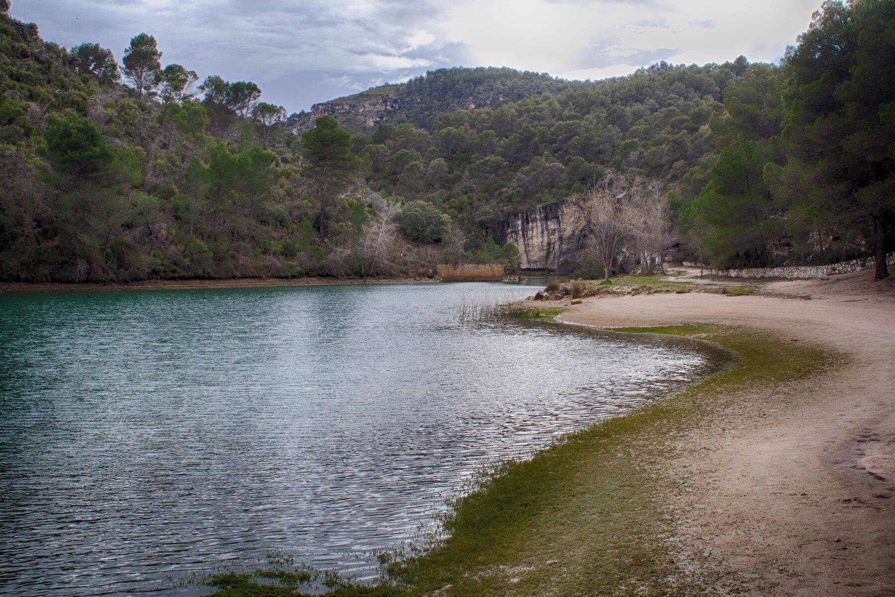 A calm lake surrounded by dense forest and a rocky cliff.