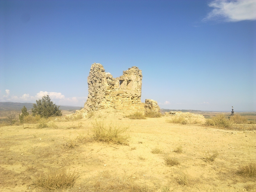 A stone ruin in a desert landscape with sparse vegetation and a clear blue sky.
