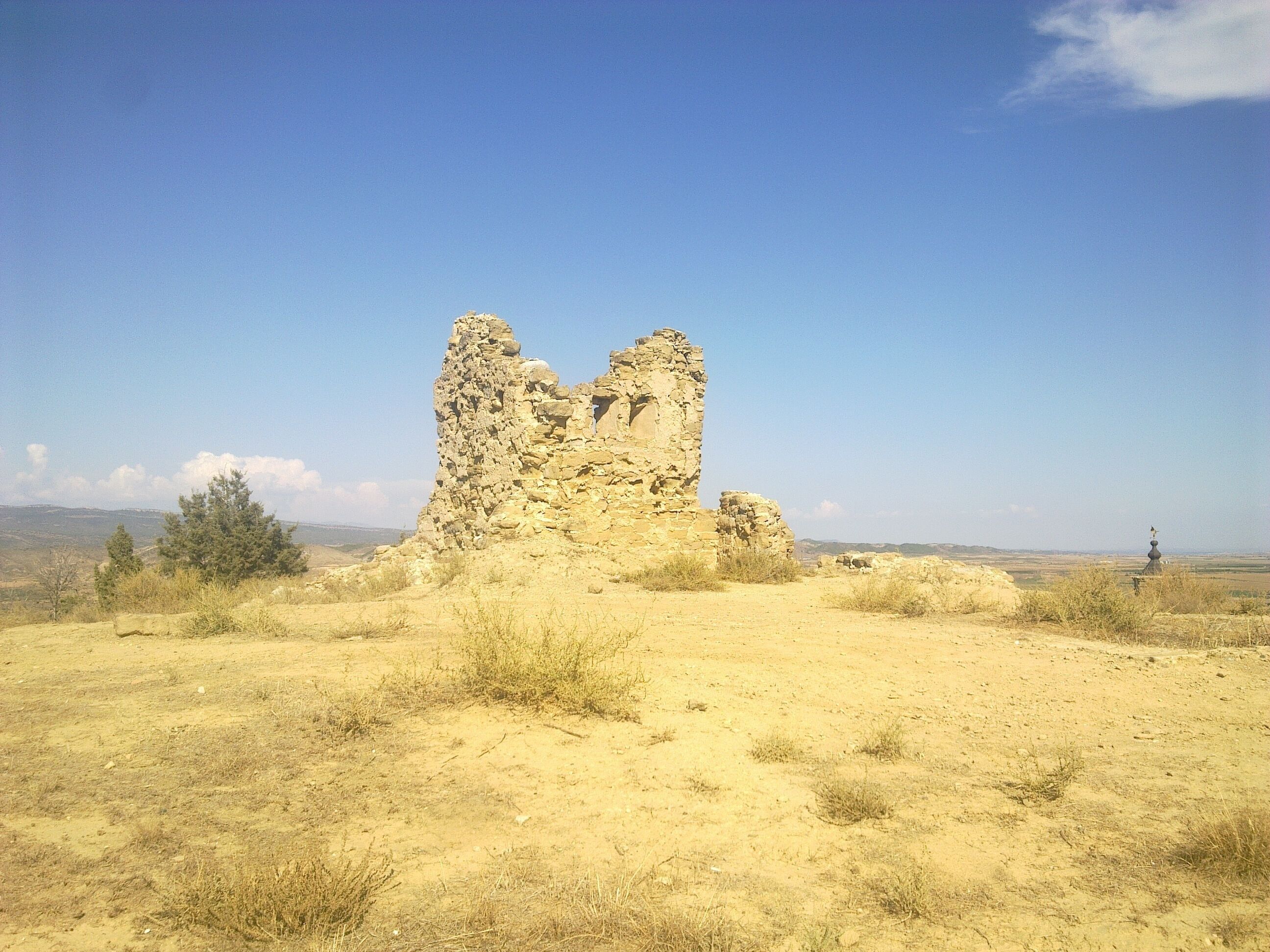 A stone ruin in a desert landscape with sparse vegetation and a clear blue sky.