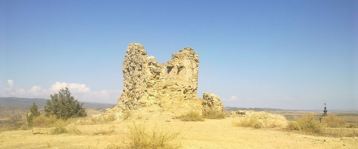 A stone ruin in a desert landscape with sparse vegetation and a clear blue sky.