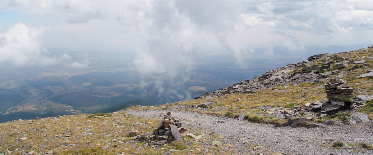 A mountainous landscape with a rocky path and a cairn.