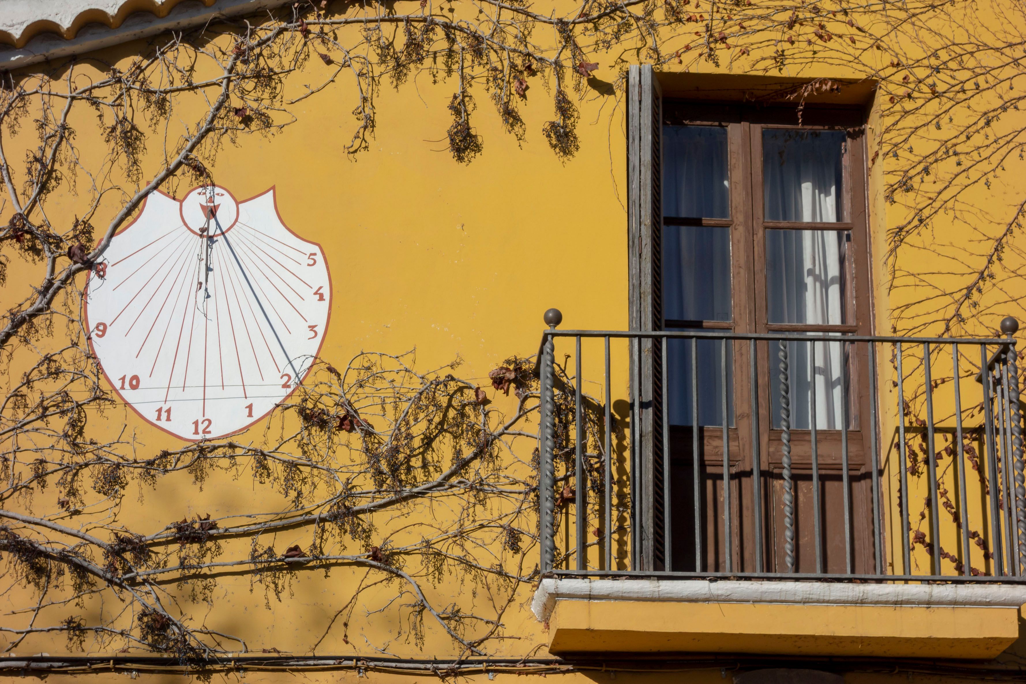 A yellow building with a large sundial and a window with a wooden shutter.