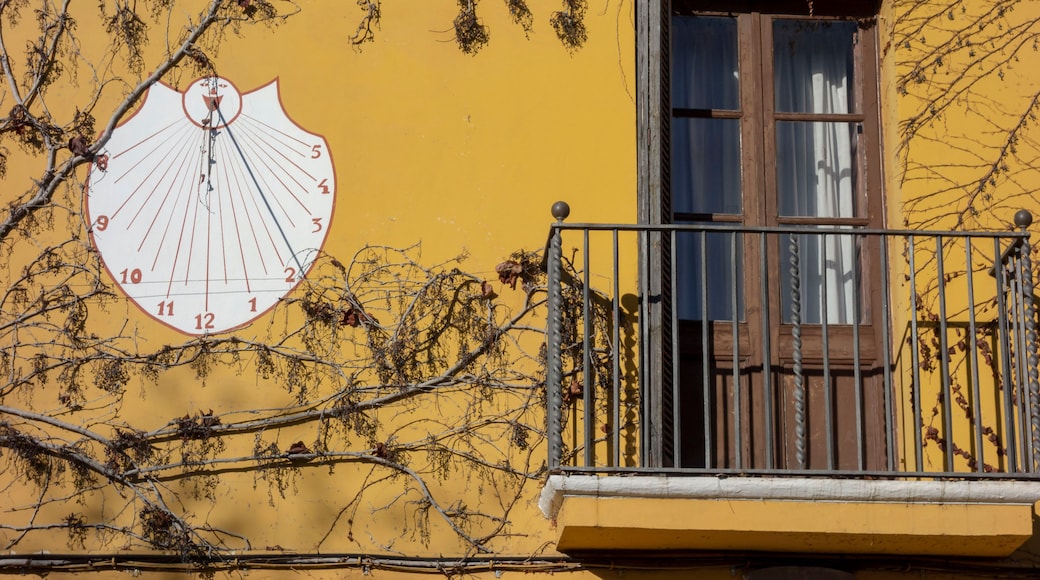 A yellow building with a large sundial and a window with a wooden shutter.