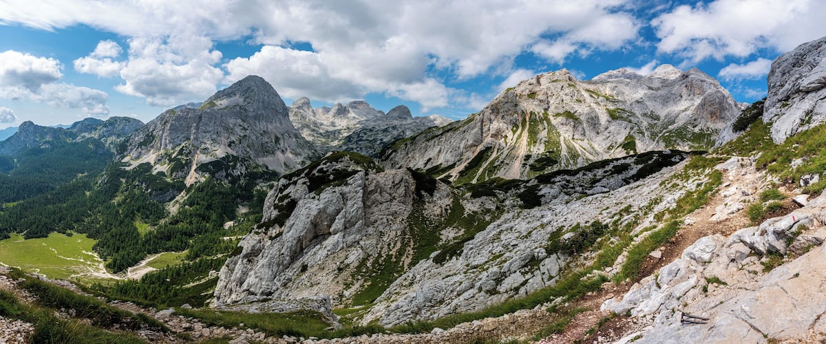 A mountainous landscape with rocky peaks, green valleys, and a clear sky.