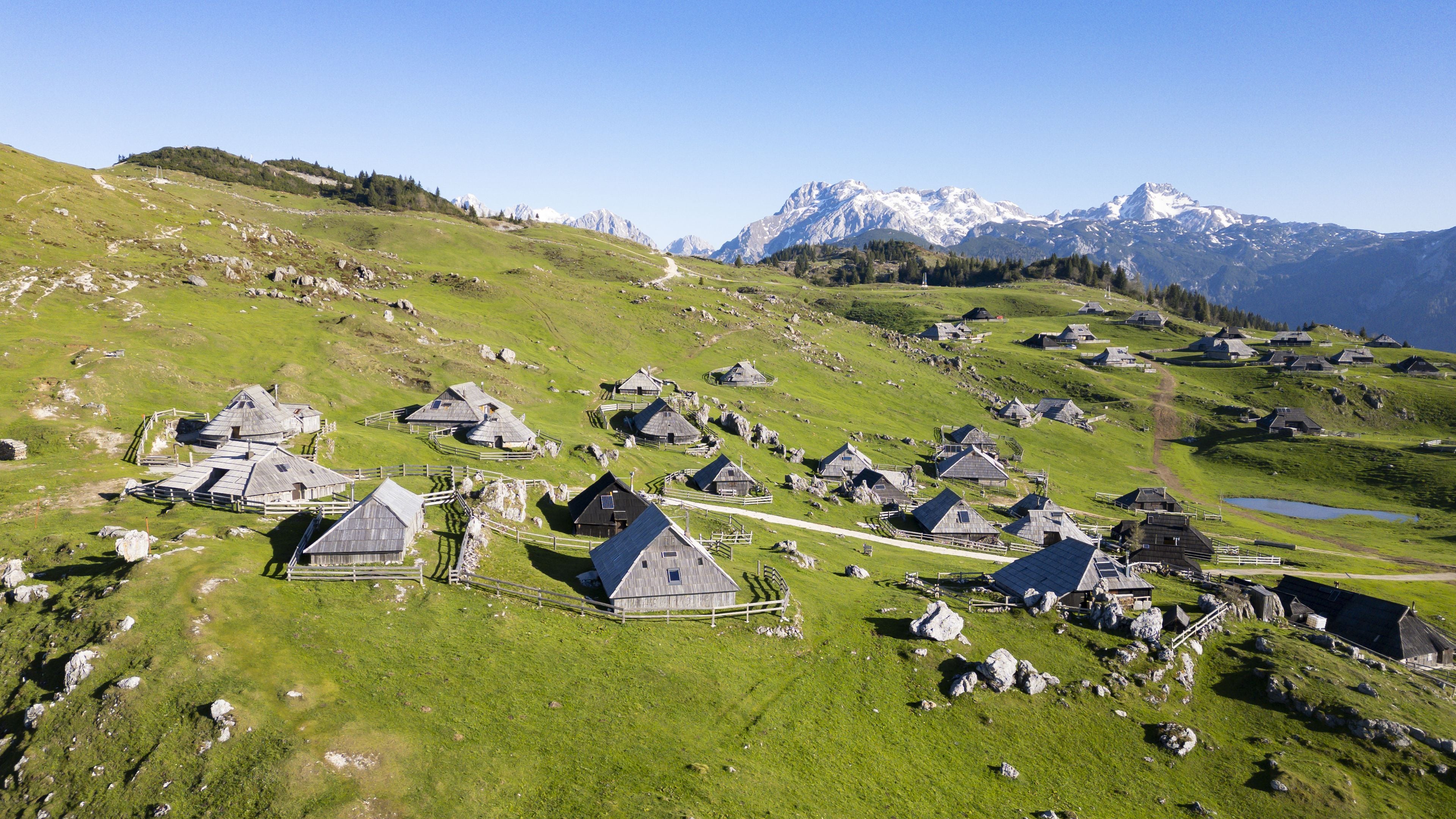 Un groupe de maisons de montagne traditionnelles, regroupées sur une colline, avec en arrière-plan des sommets enneigés.